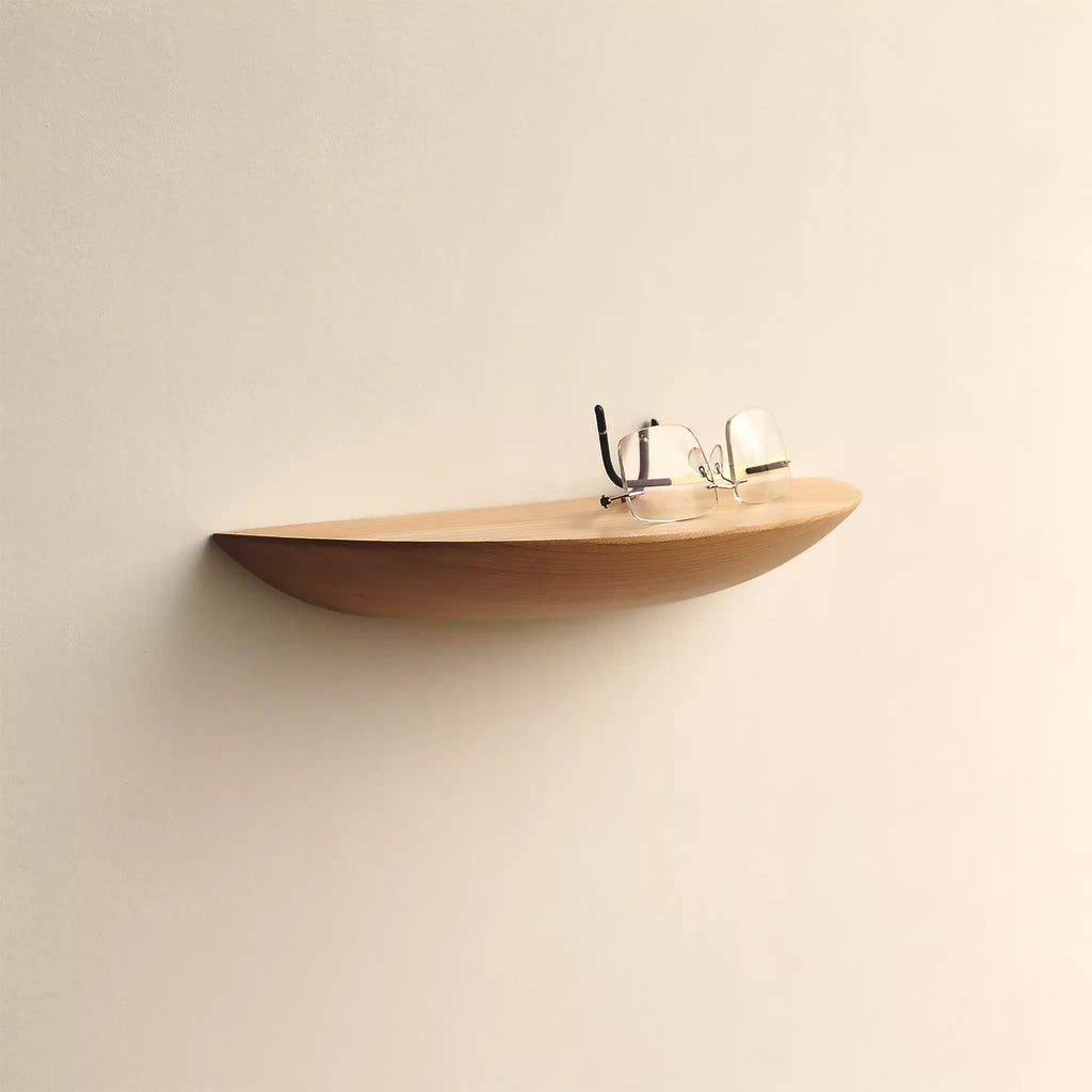 Half moon ash shelf mounted on a pale wall with a pair of glasses resting in the hollow