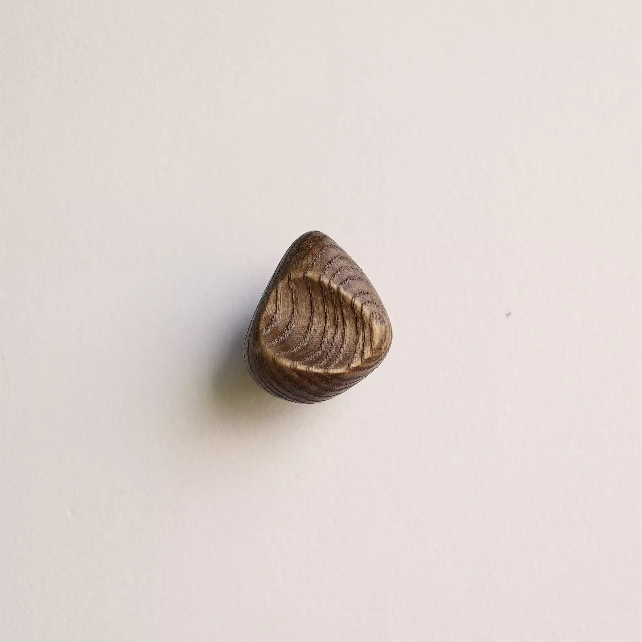 Shell hook in the walnut finish, mounted on a pale wall
