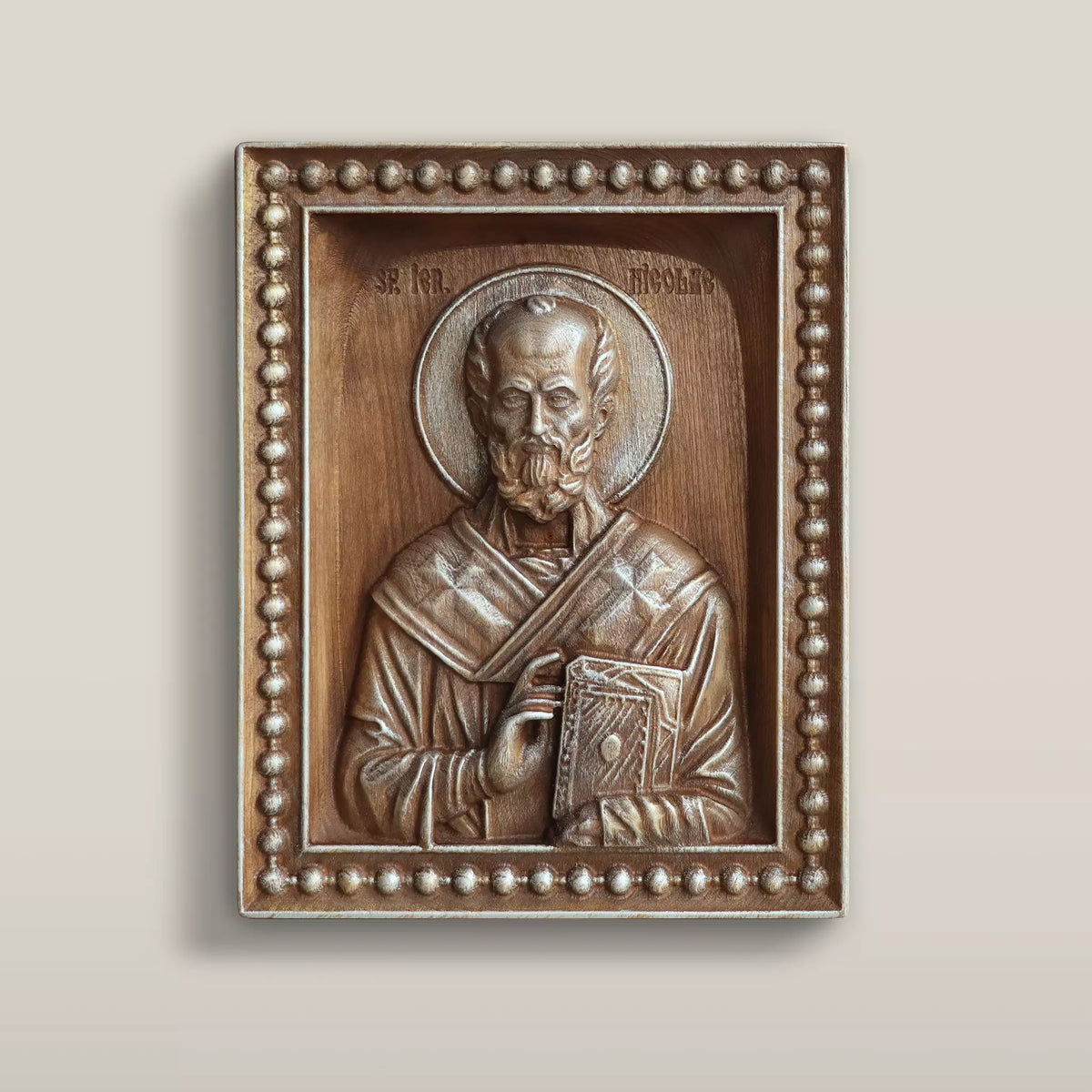 Carved wooden icon of Saint Nicholas blessing and holding the Gospel book, set within a carved beaded border