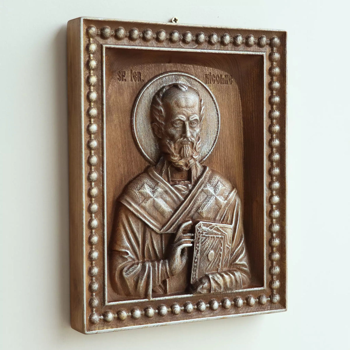 The icon seen at an angle on a white wall, showing the depth of the carved frame