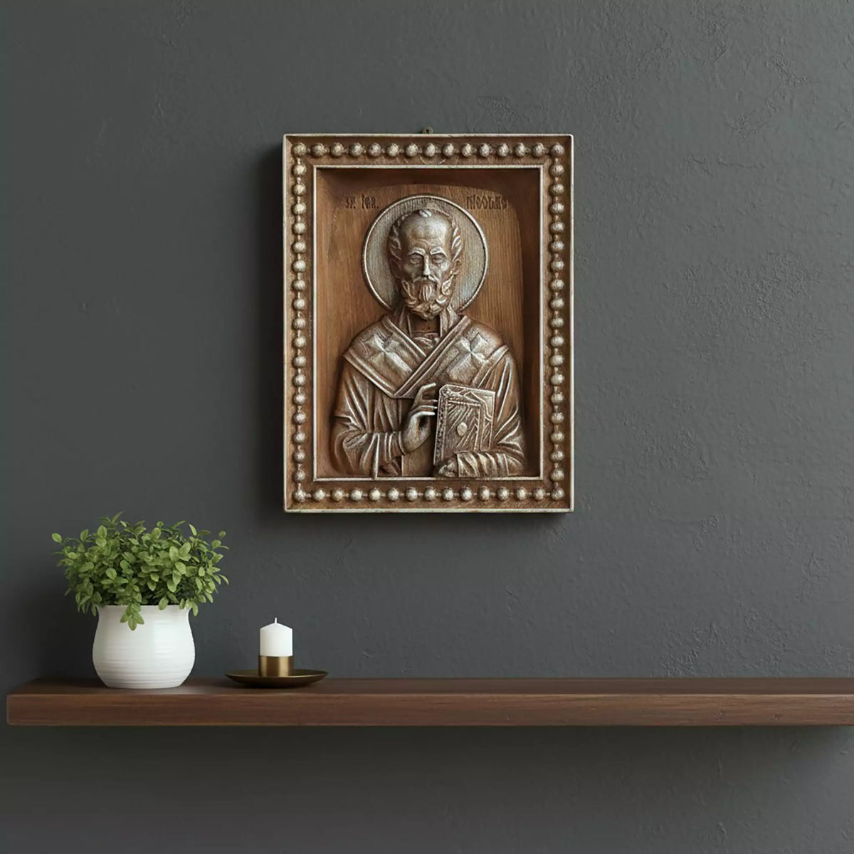 The icon hung on a dark grey wall above a floating shelf with a plant and a candle