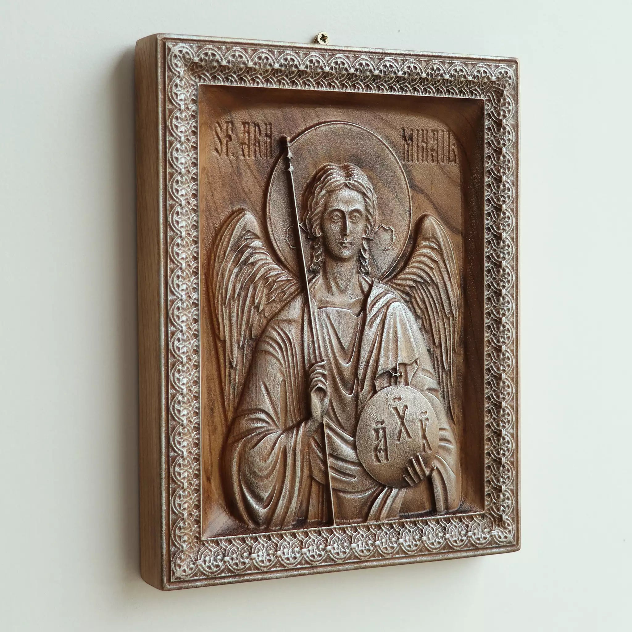 Carved wood icon of the Archangel Michael seen at an angle from above, with light raking across the carving