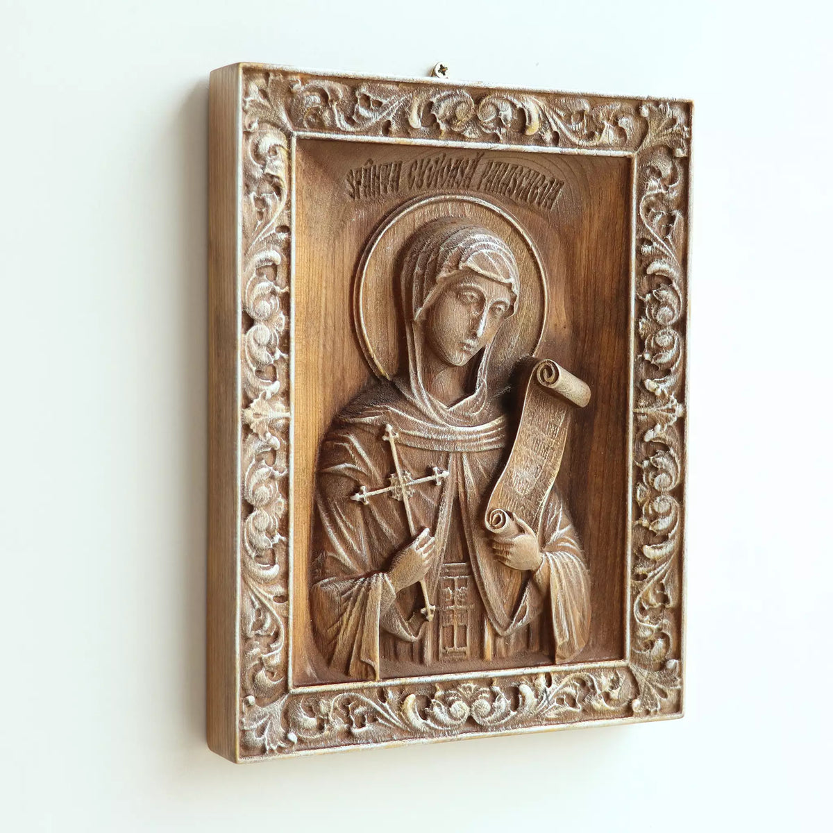 The icon seen at an angle on a white wall, showing the depth of the carved frame