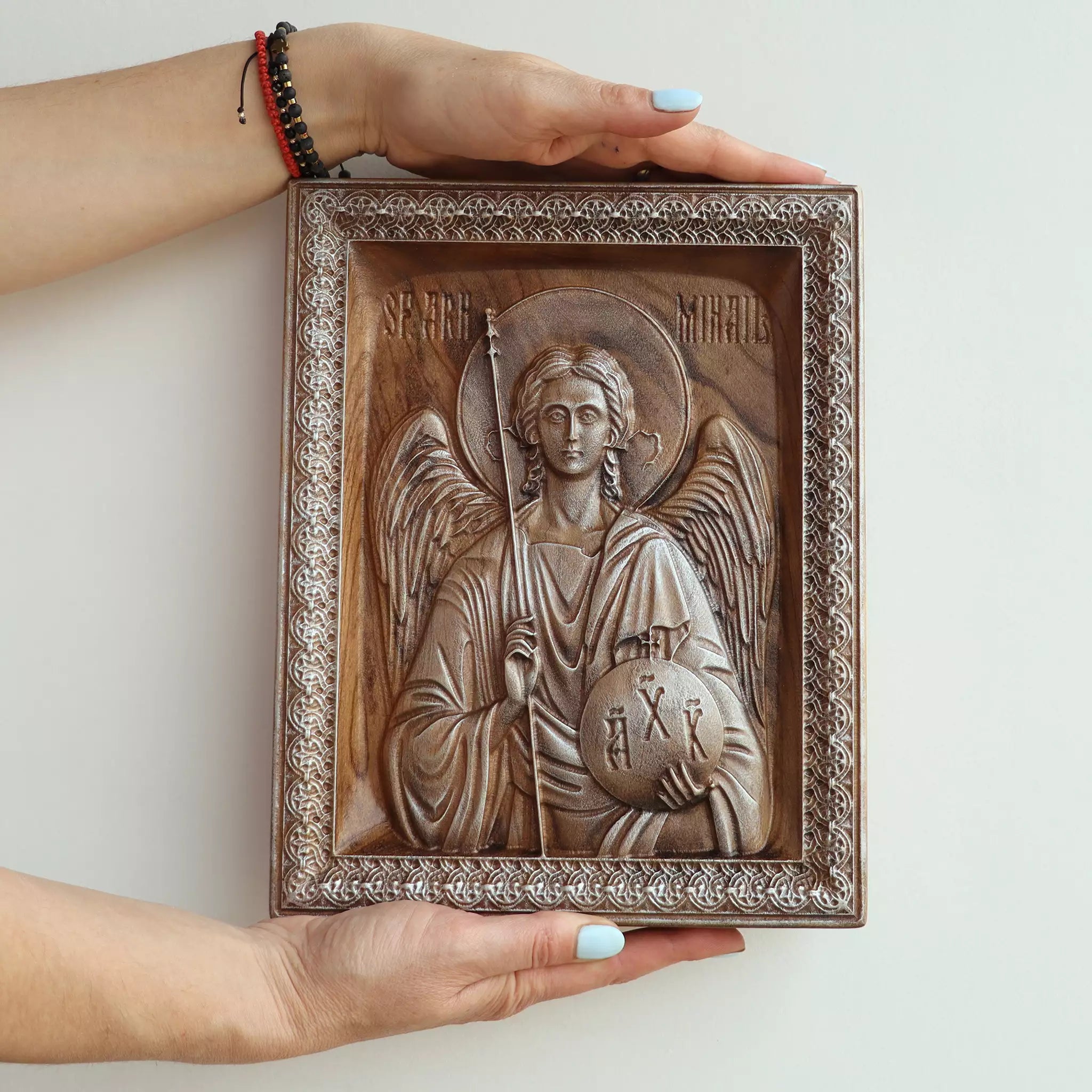 Two hands holding the carved wood icon of the Archangel Michael, showing its size against a person