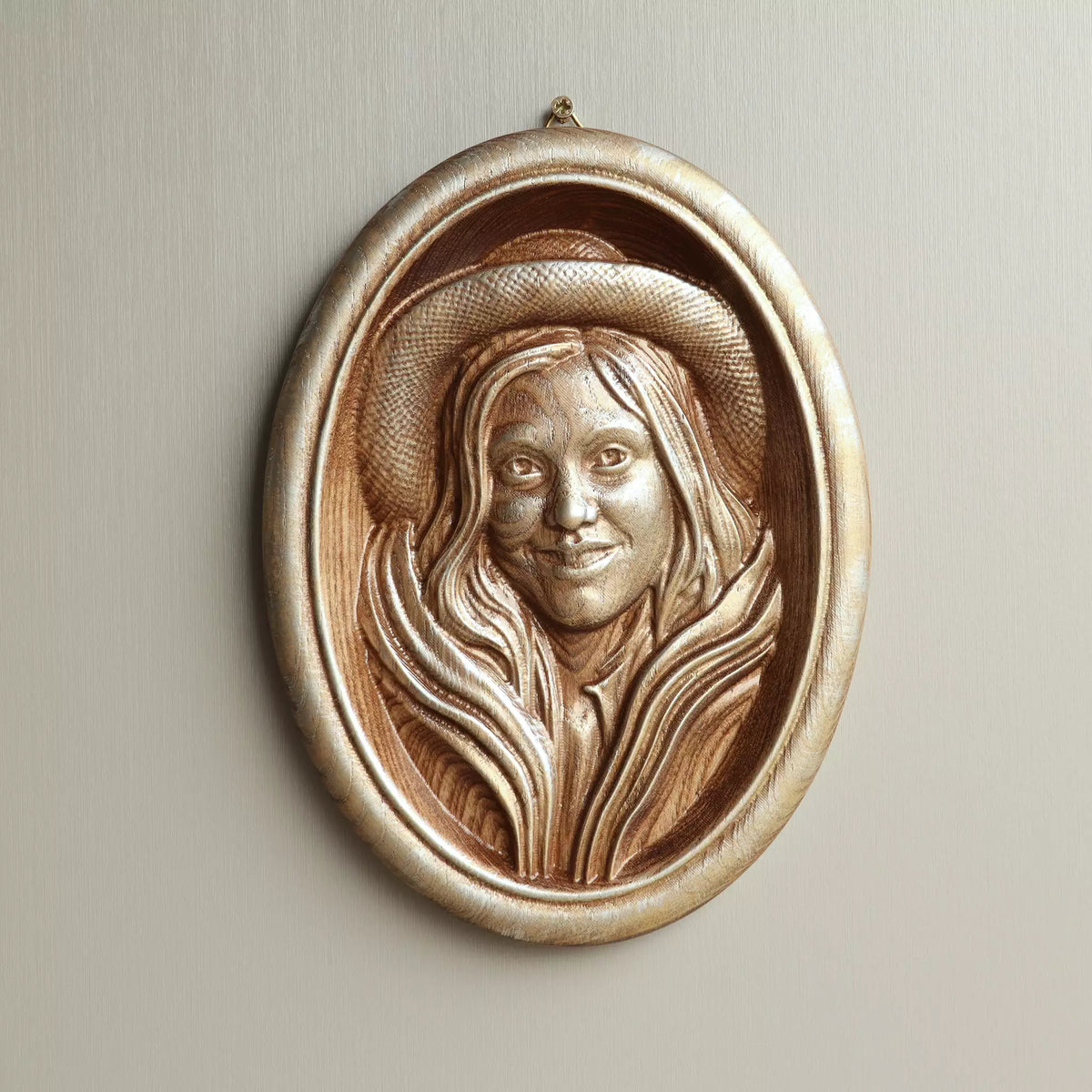 Carved oval wood portrait in the walnut and gold-silver patina finish, hanging on a pale wall