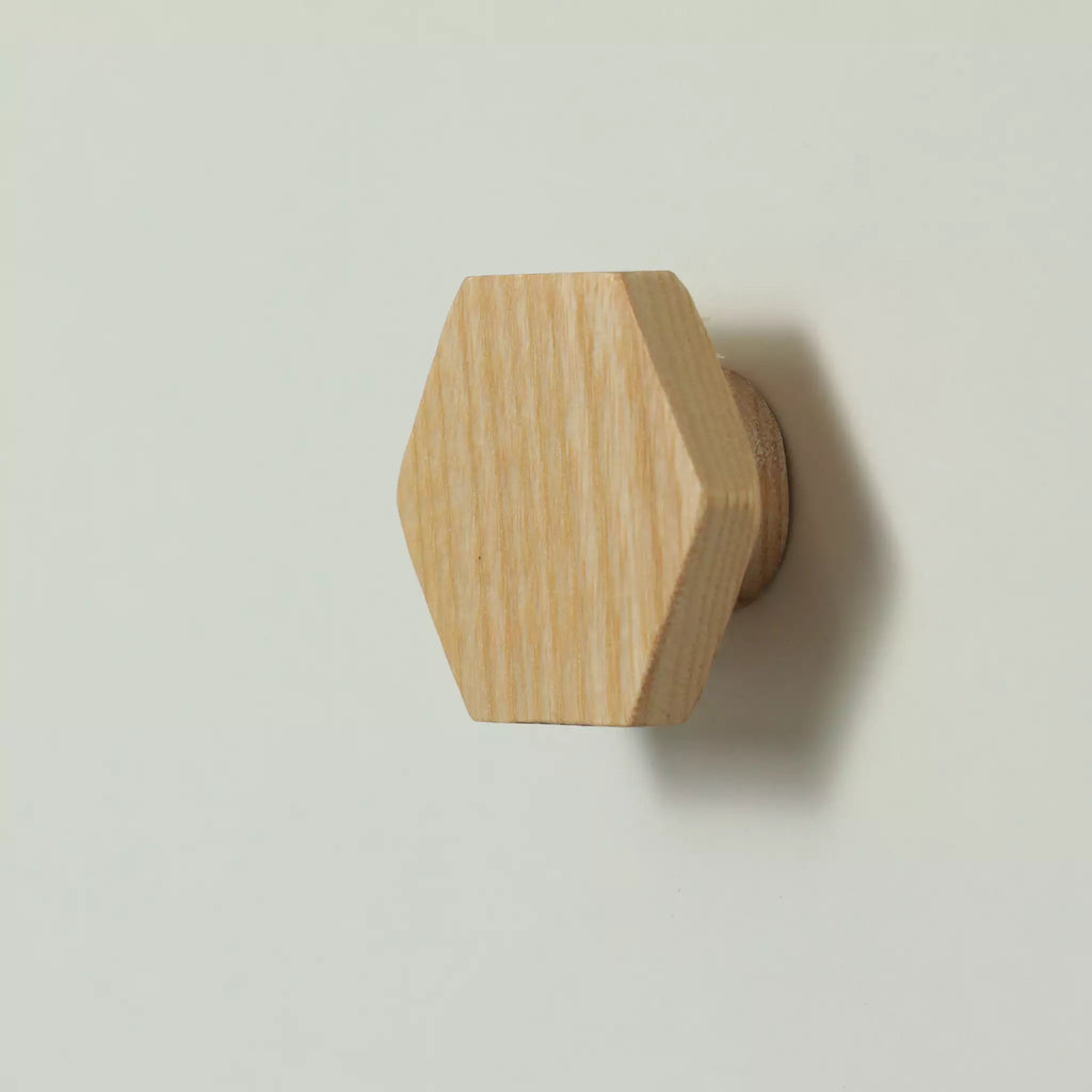 Unfinished solid ash hexagon cabinet knob seen from the side, with the base visible behind it