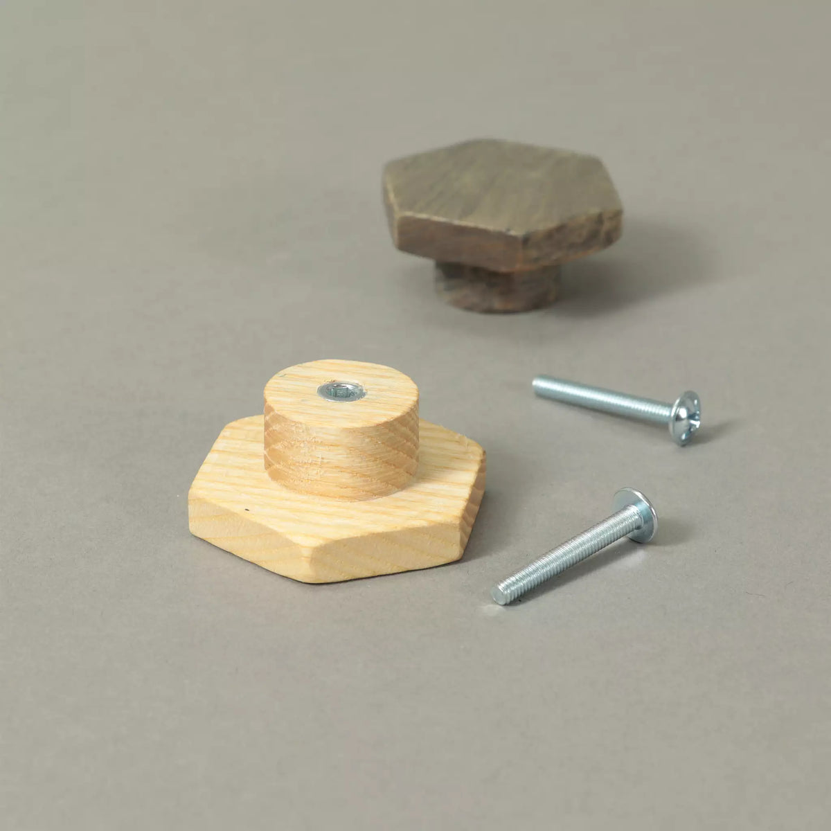 Back of an unfinished hexagon cabinet knob showing the base and the threaded metal insert, with a Dark Gray knob and the mounting hardware behind
