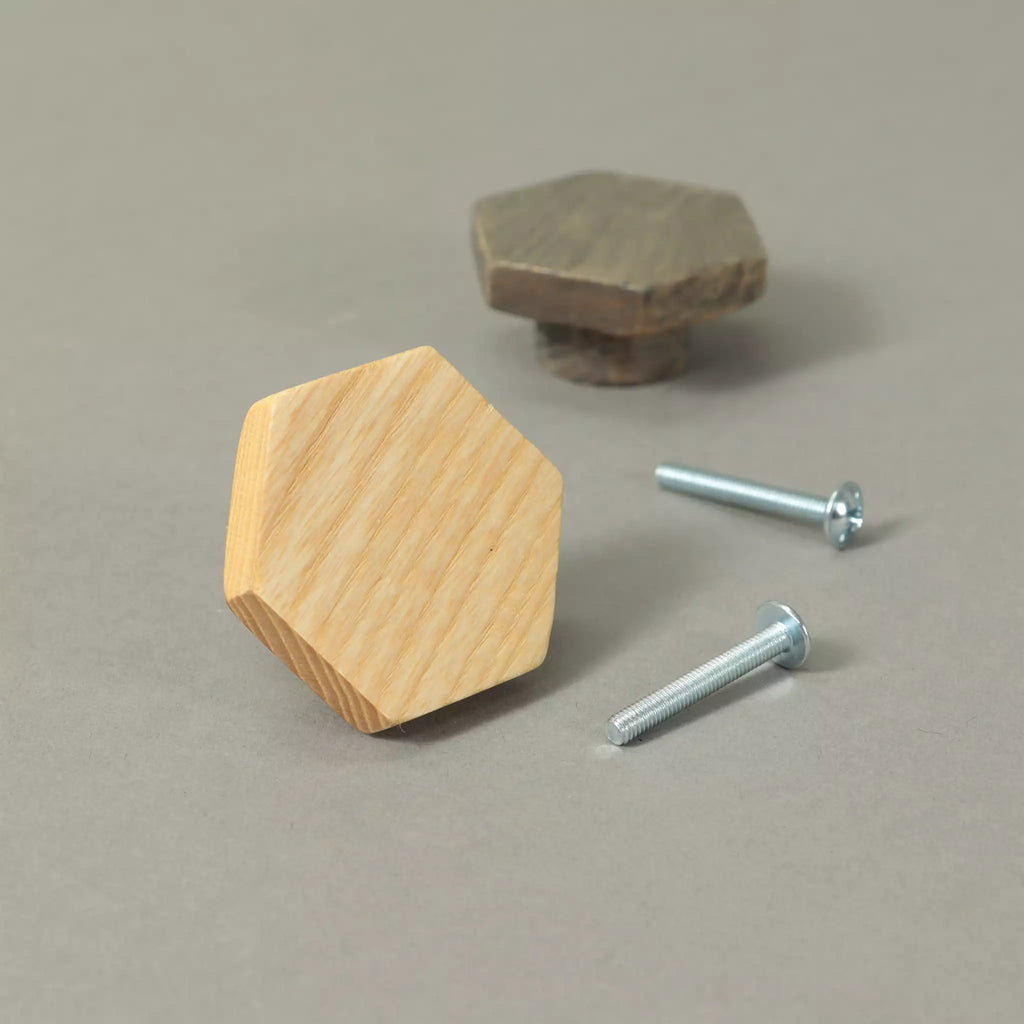 Unfinished and Dark Gray hexagon cabinet knobs beside the mounting hardware, on a grey background