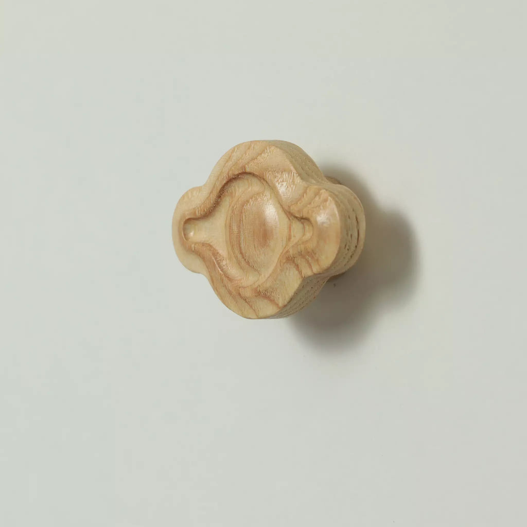 Unfinished solid ash petal cabinet knob seen at an angle, with the base visible behind it