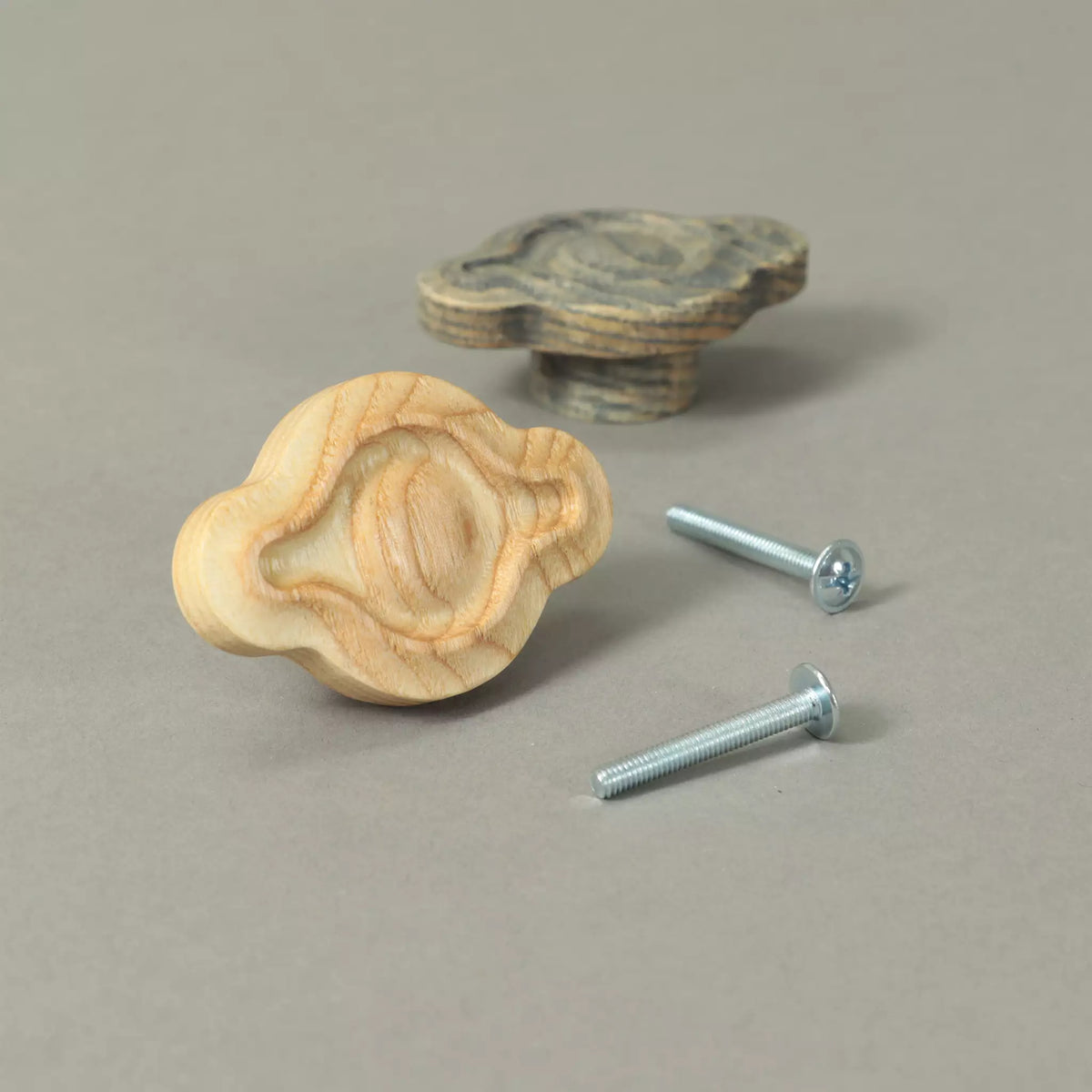 Unfinished and Dark Gray petal cabinet knobs beside the mounting hardware, on a grey background