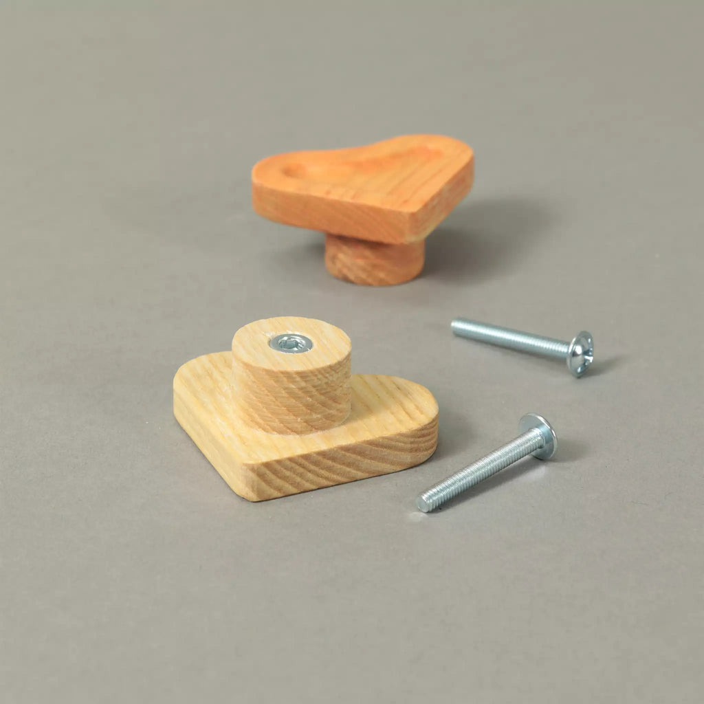 Back of an unfinished scooped heart cabinet knob showing the base and the threaded metal insert, with an Orange knob and the mounting hardware behind