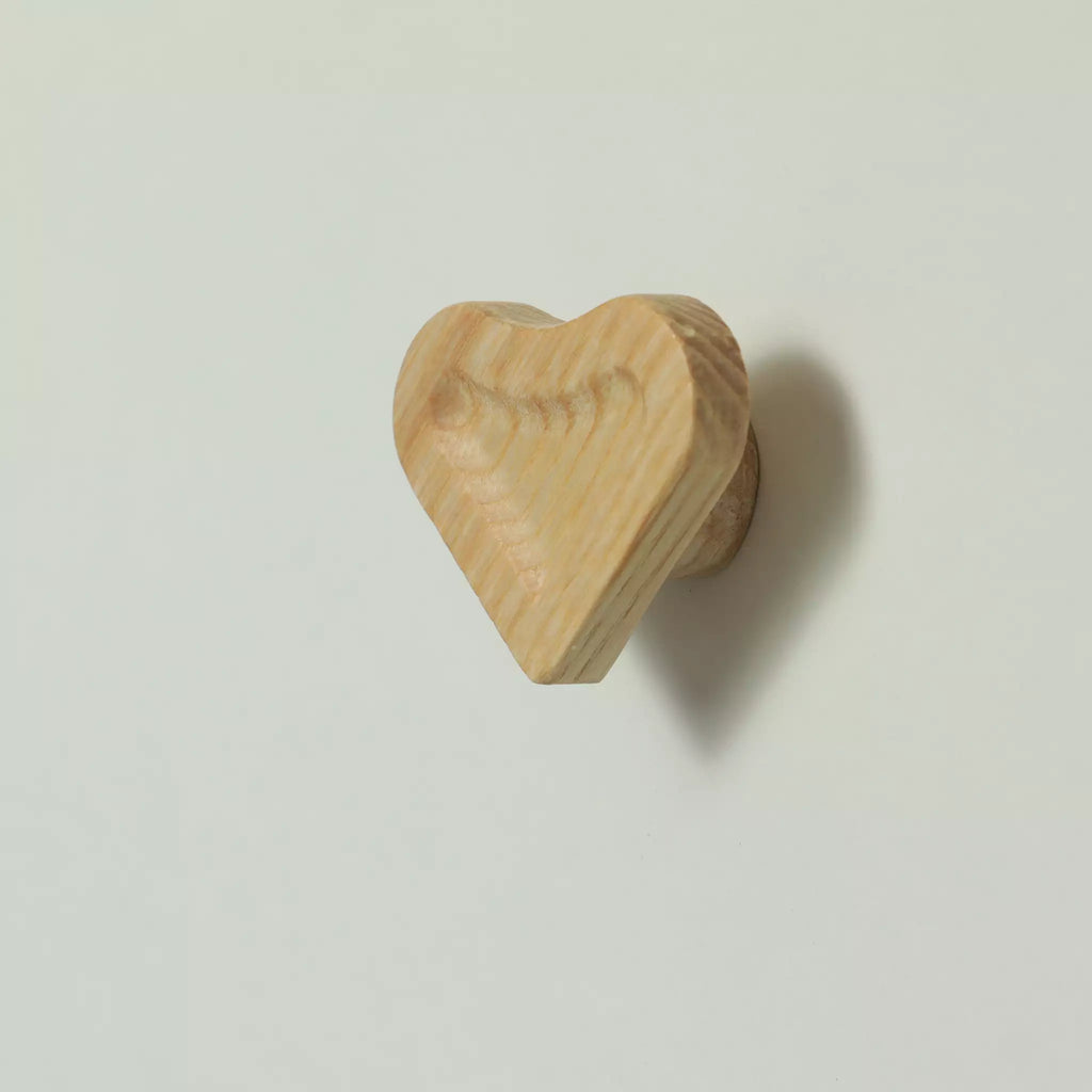 Unfinished solid ash scooped heart cabinet knob seen at an angle, with the base visible behind it
