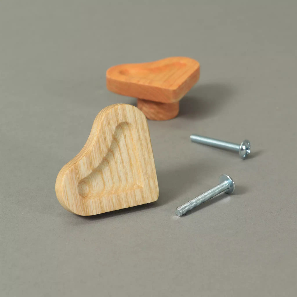 Unfinished and Orange scooped heart cabinet knobs beside the mounting hardware, on a grey background