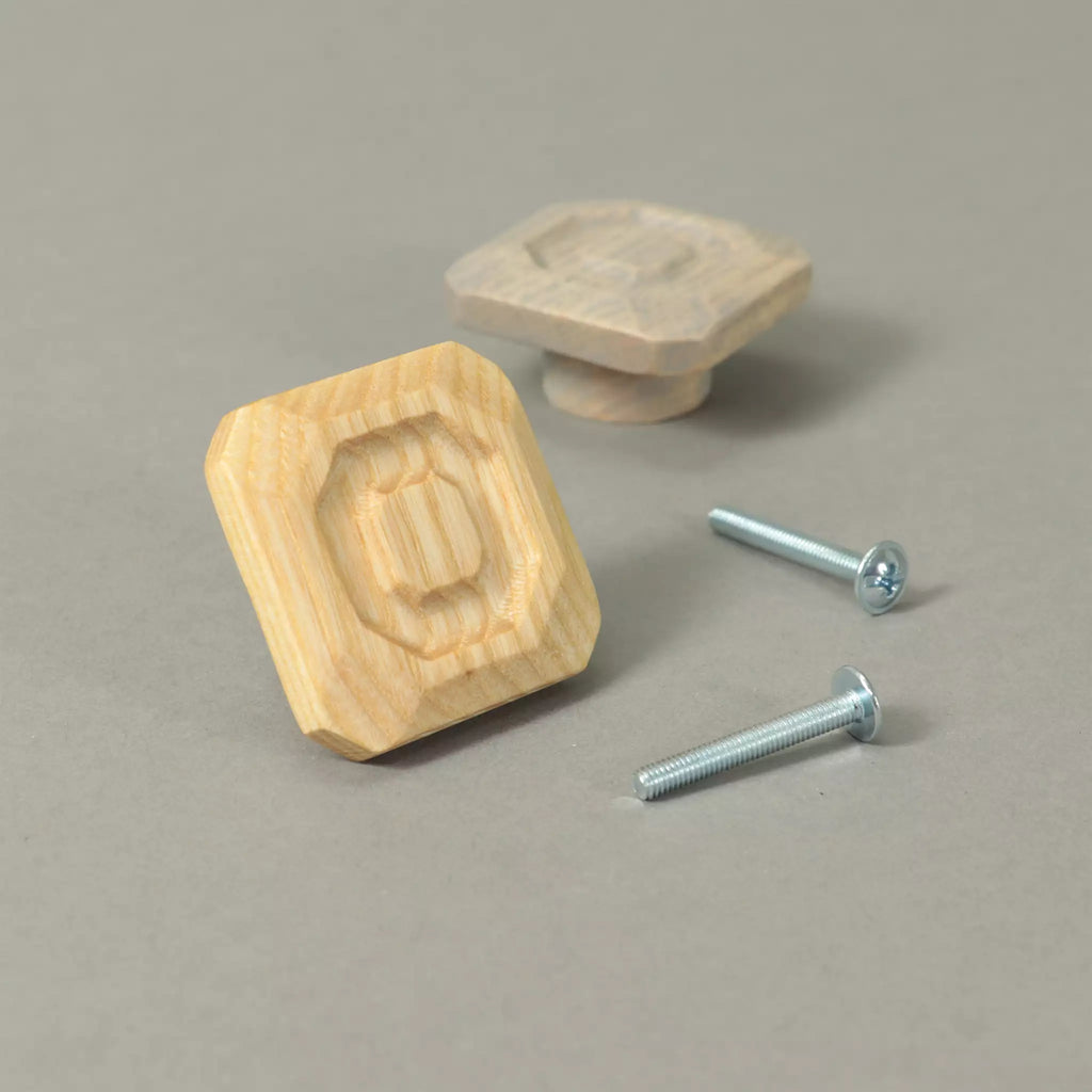 Two stepped octagon cabinet knobs in solid ash beside the mounting hardware, on a grey background
