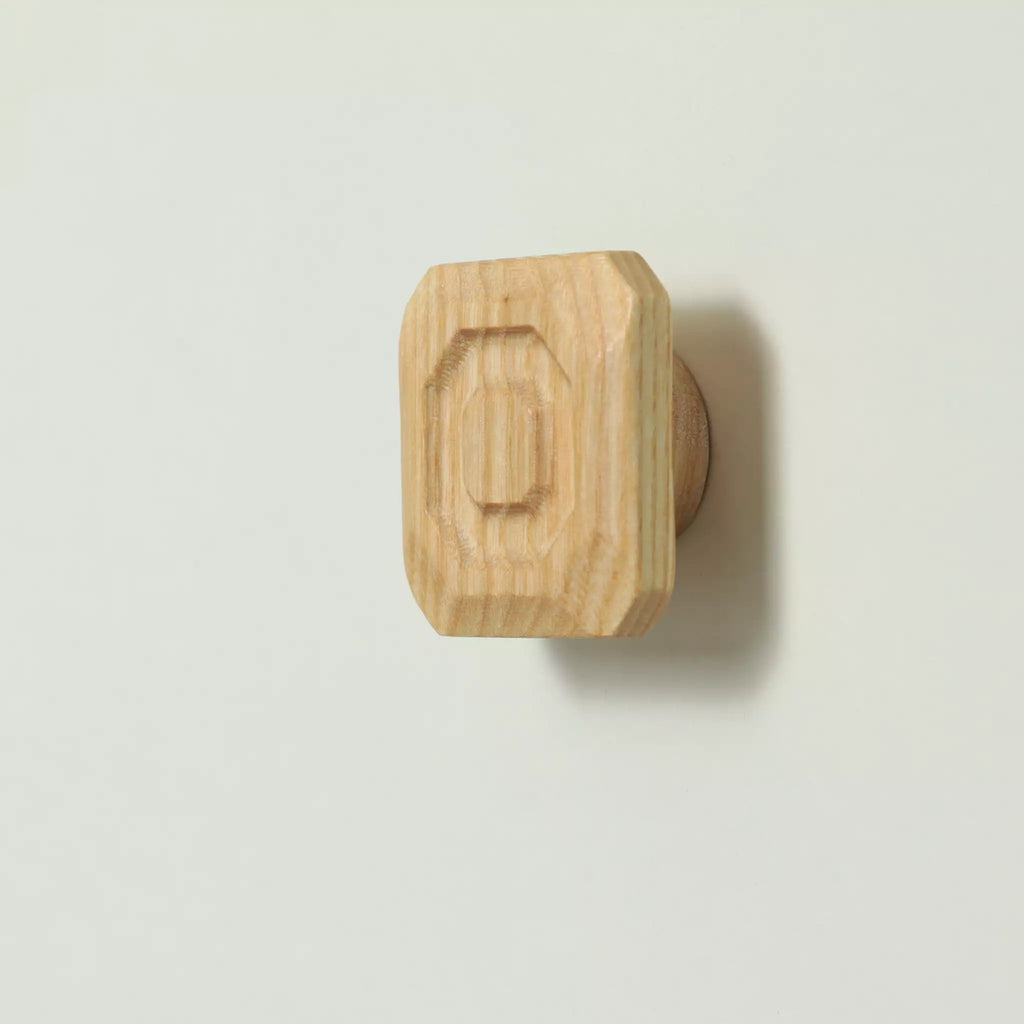 Unfinished solid ash stepped octagon cabinet knob seen at an angle, with the base visible behind it