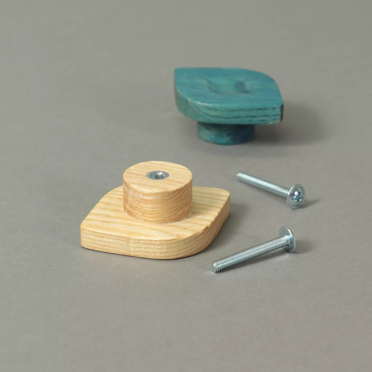 Back of an unfinished twist cabinet knob showing the base and the threaded metal insert, with a Blue knob and the mounting hardware behind