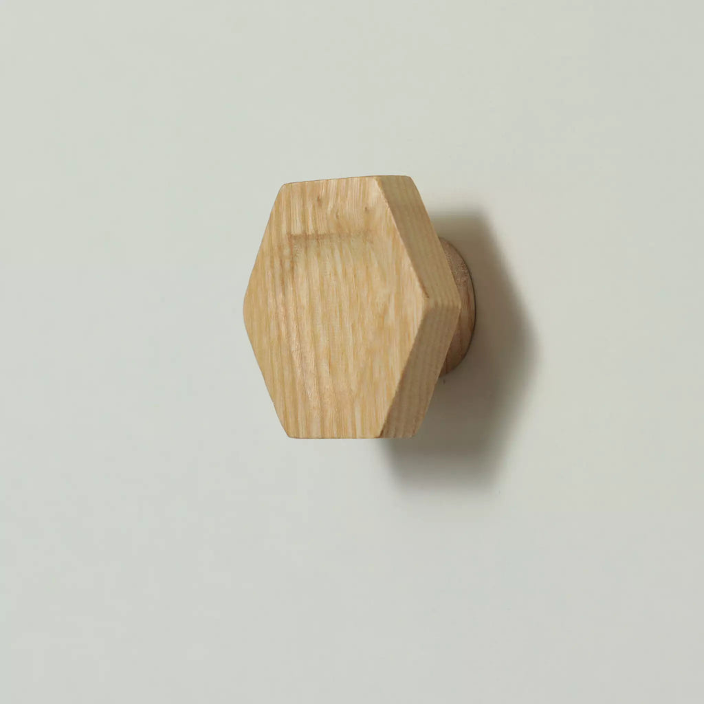 Unfinished solid ash carved hexagon cabinet knob seen from the side, with the base visible behind it