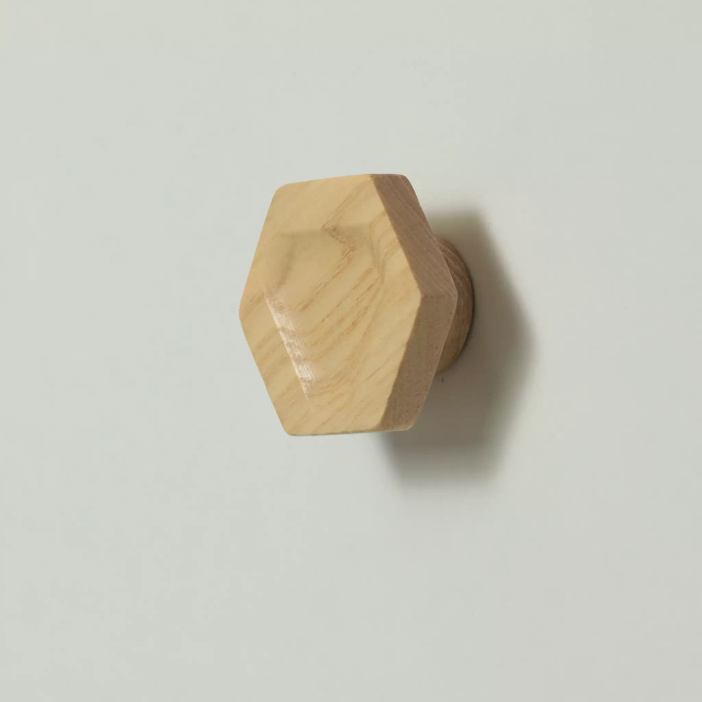 Unfinished solid ash carved hexagon cabinet knob seen at an angle, showing the thickness of the block