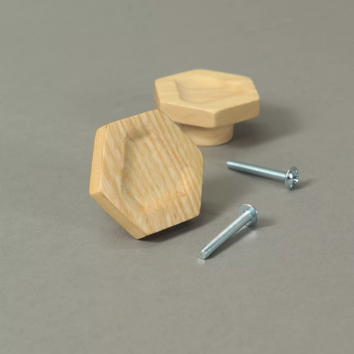 Two carved hexagon cabinet knobs in solid ash beside the mounting hardware, on a grey background