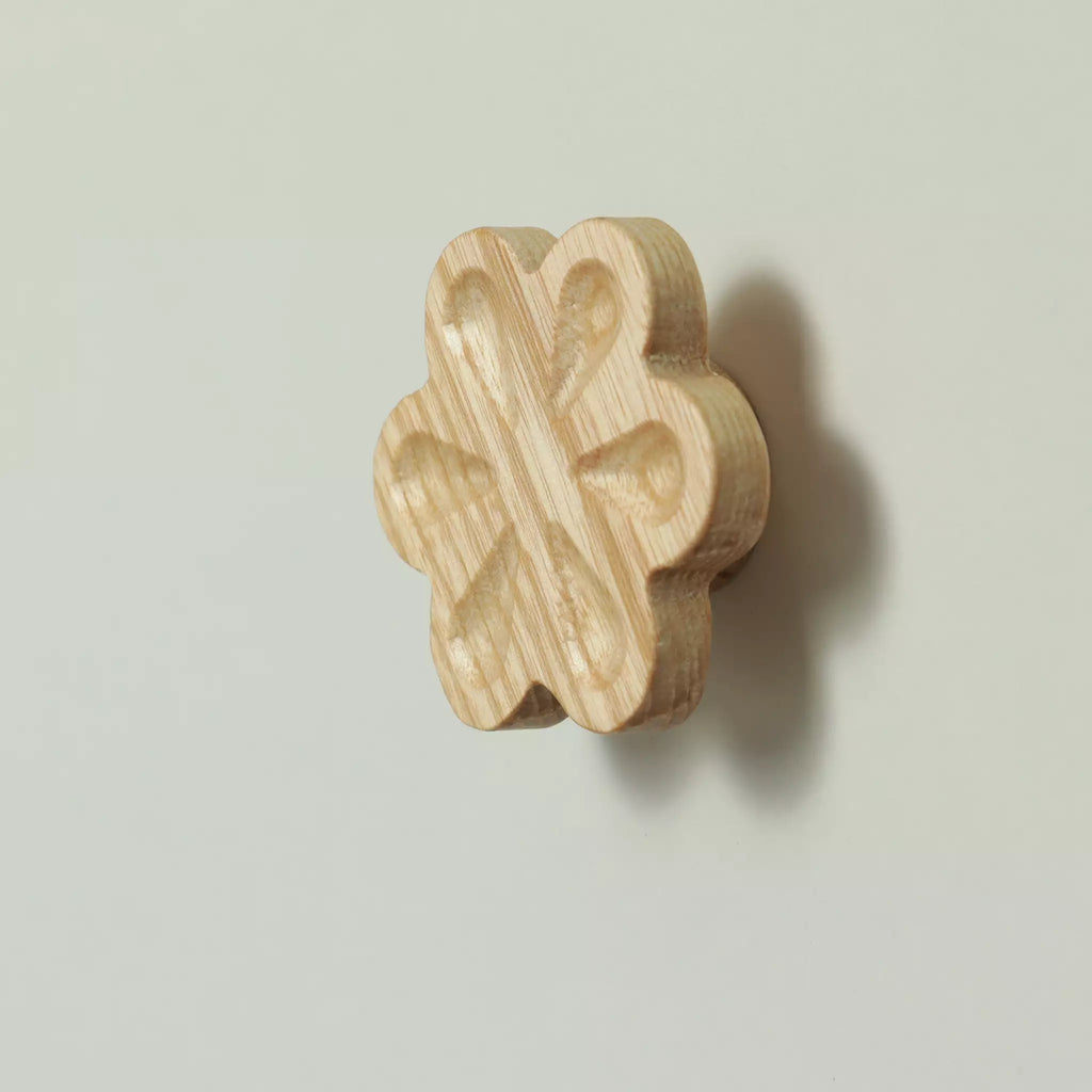 Unfinished solid ash carved flower cabinet knob seen at an angle, with the base visible behind it