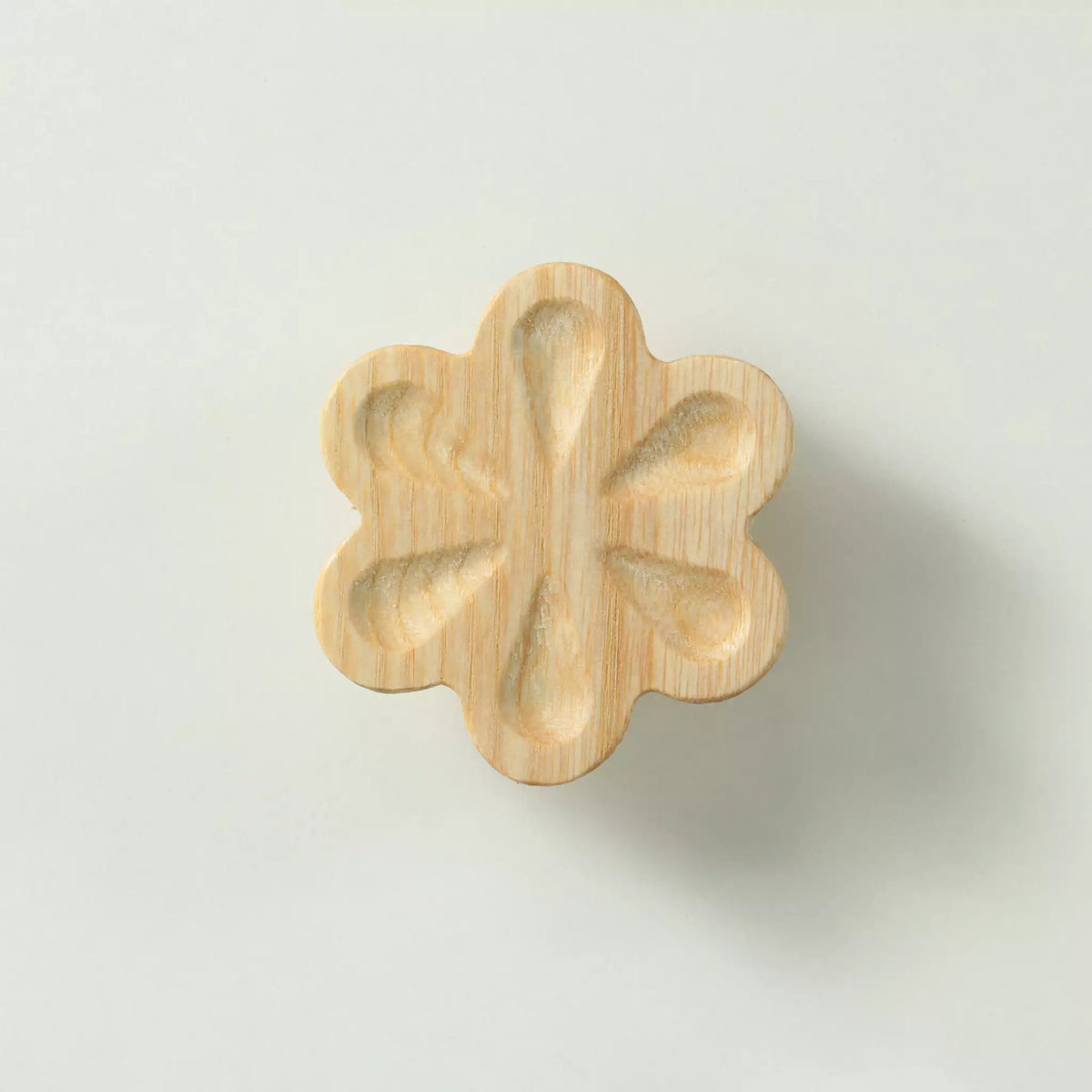 Unfinished solid ash carved flower cabinet knob seen from the front, showing the six hollowed petals