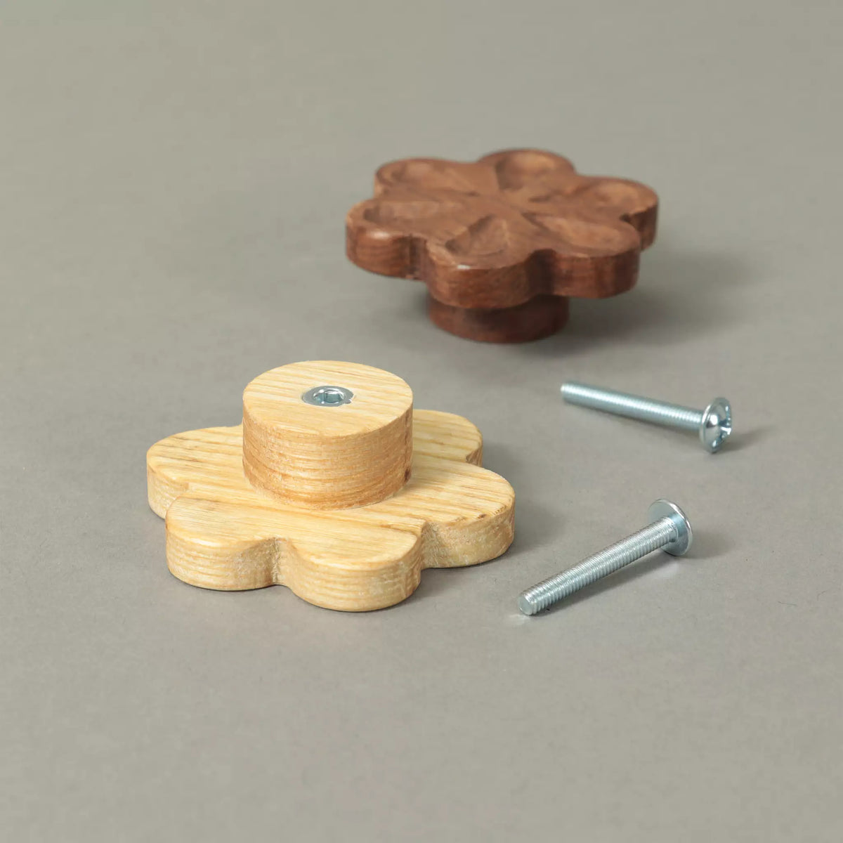 Unfinished and Walnut carved flower cabinet knobs beside the mounting hardware, on a grey background