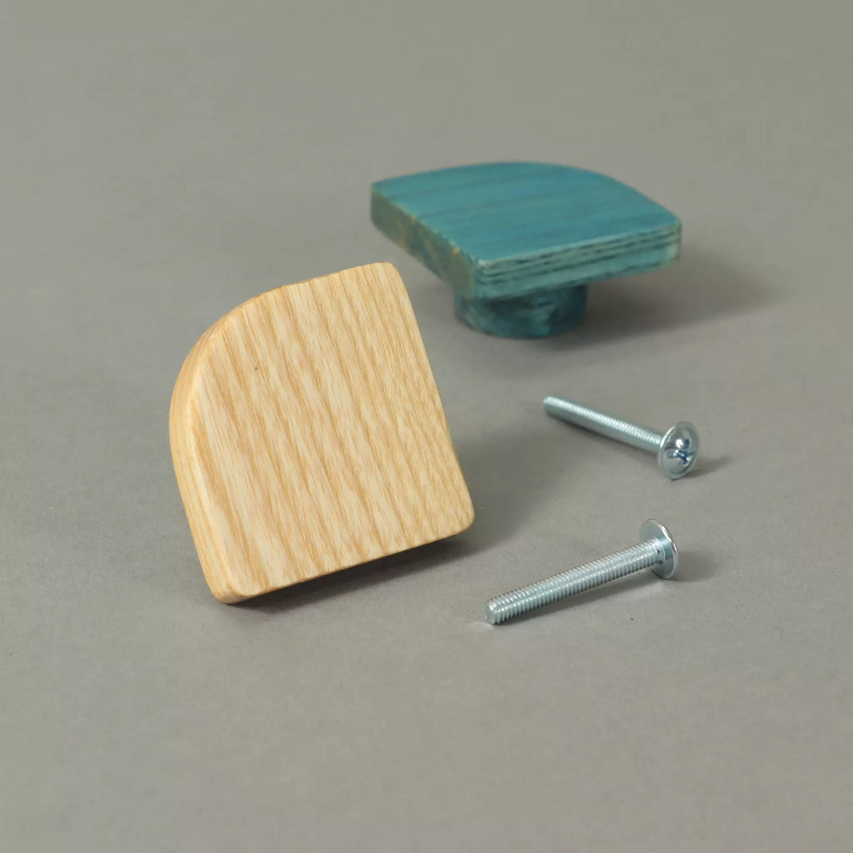 Two fan-shaped ash cabinet knobs with their mounting screws, one in bare wood and one in Blue