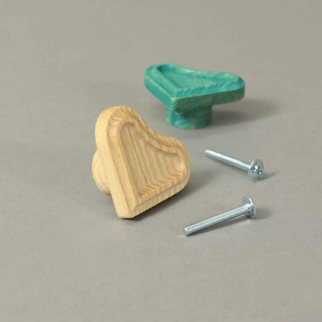 Unfinished and Green heart cabinet knobs beside the mounting hardware, on a grey background