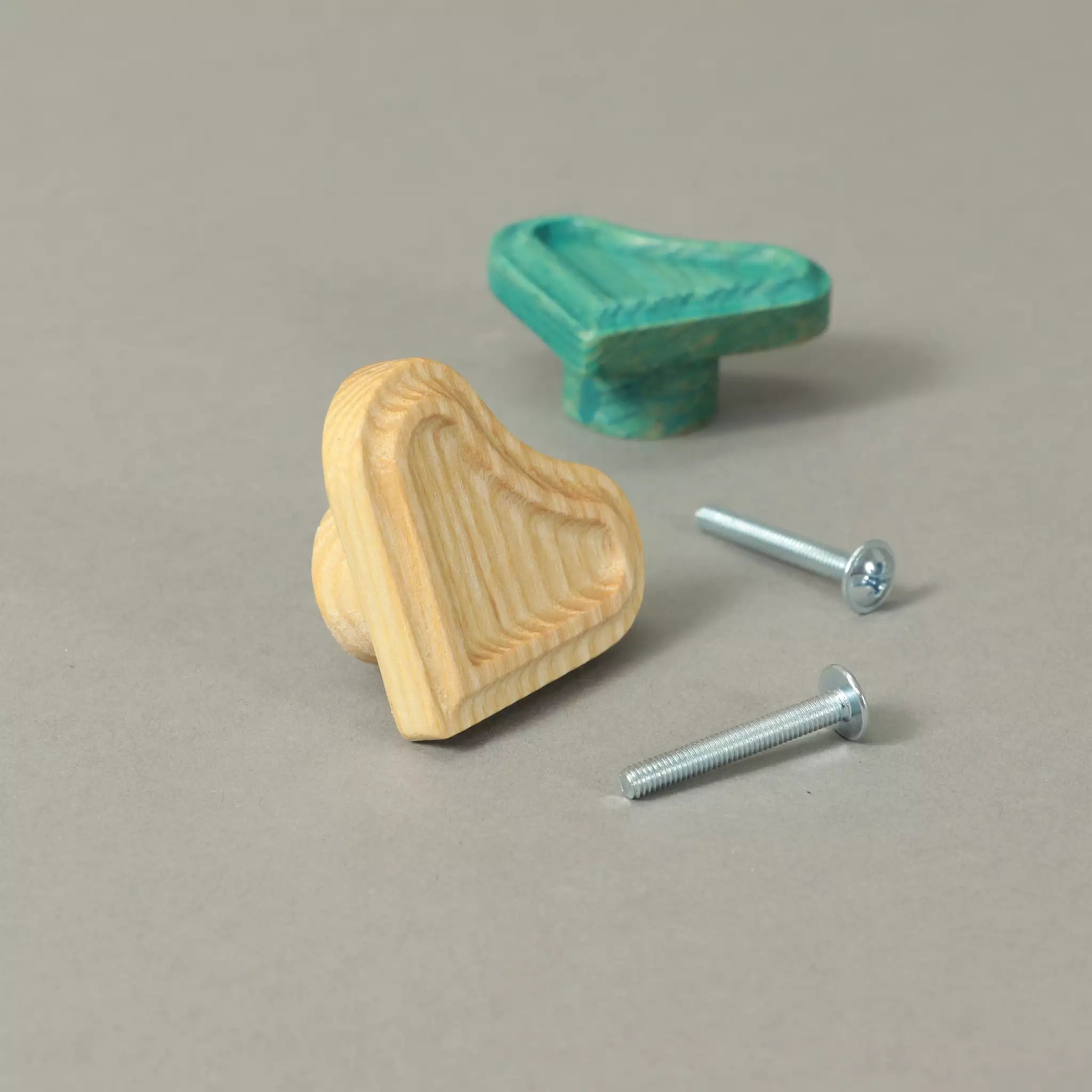Unfinished and Green heart cabinet knobs beside the mounting hardware, on a grey background