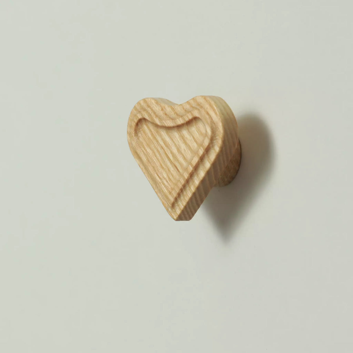 Unfinished solid ash heart cabinet knob seen from the front with the base visible behind it