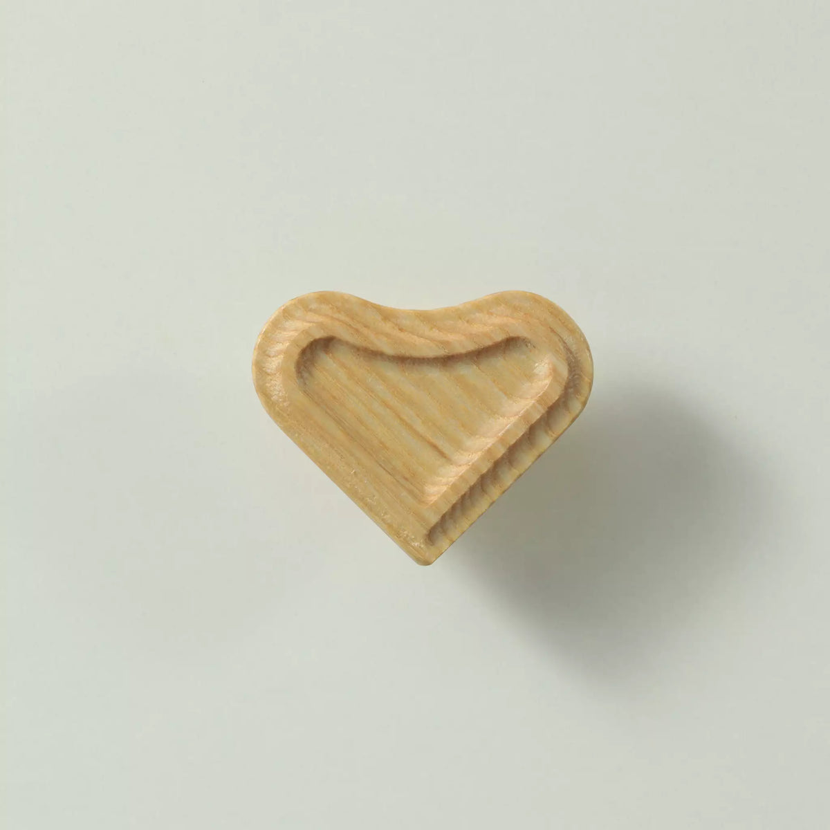 Unfinished solid ash heart cabinet knob seen at an angle, showing the recessed face