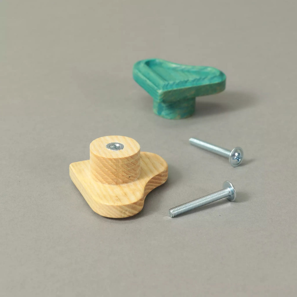 Back of an unfinished heart cabinet knob showing the base and the threaded metal insert, with a Green knob and the mounting hardware behind