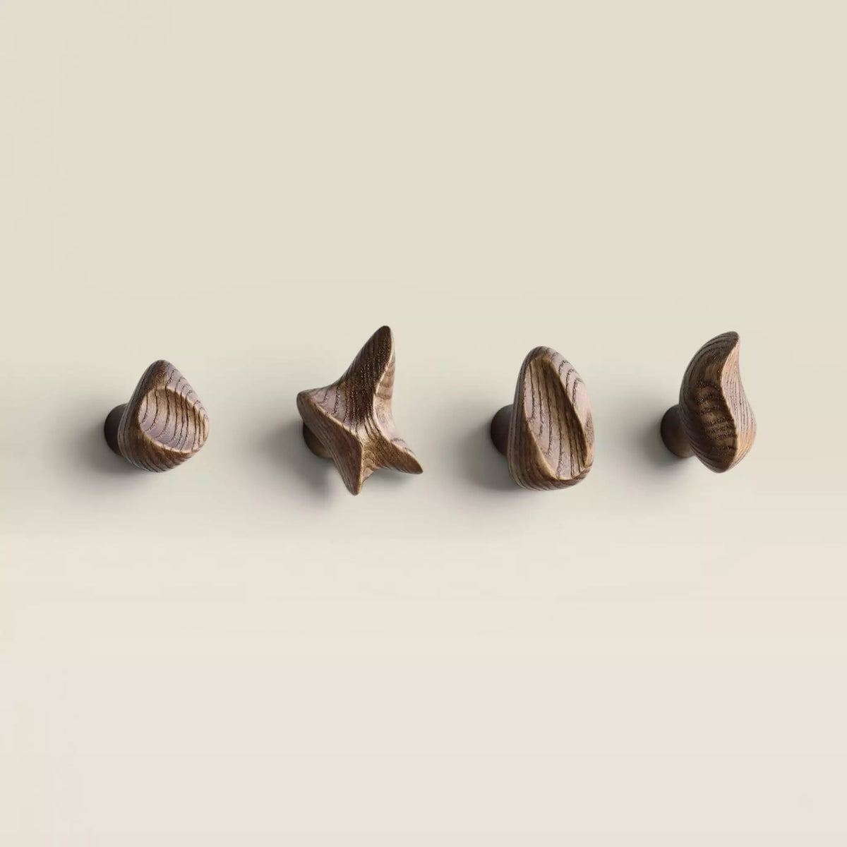 Four ash wall hooks mounted in a row on a pale wall, in the walnut finish